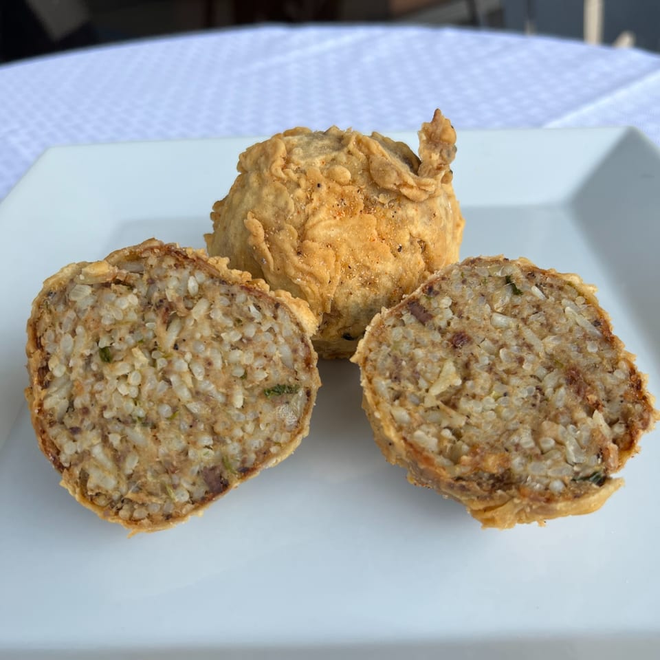 DezMeaux's Boudin: One whole and two halved fried boudin balls on a white plate.