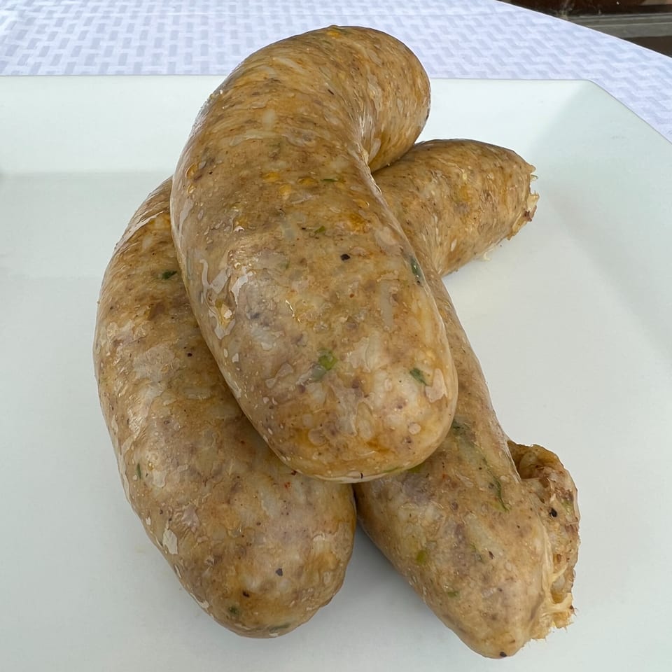 Three large, uncooked DezMeaux's Boudin sausages on a white plate with a patterned tablecloth.