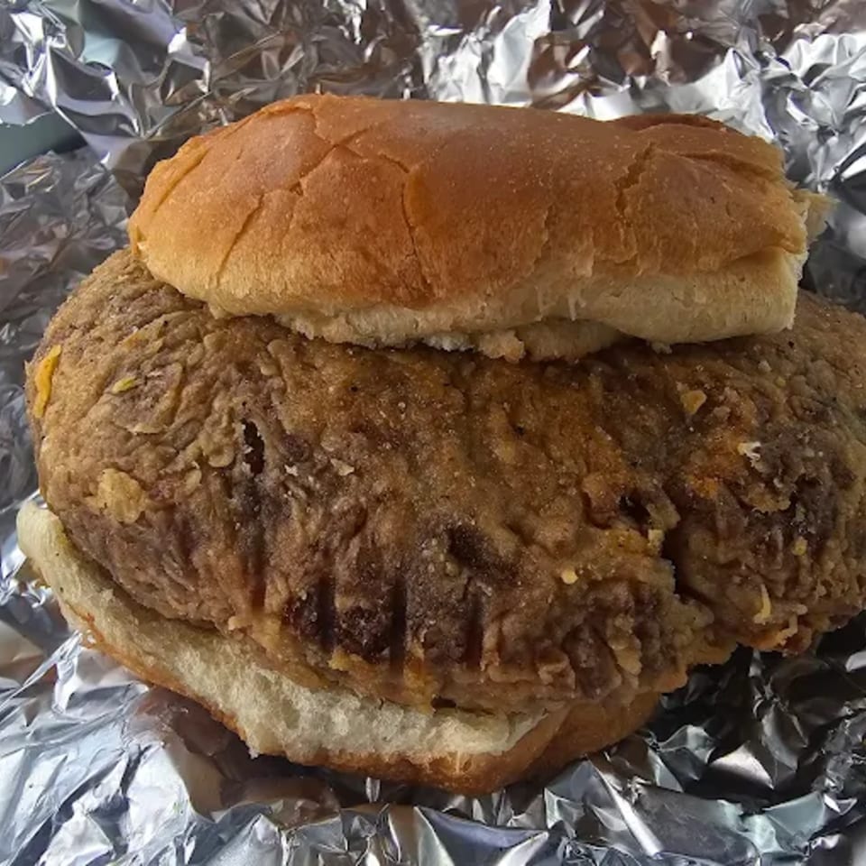 A large, crispy fried boudin patty on a bun, wrapped in aluminum foil.