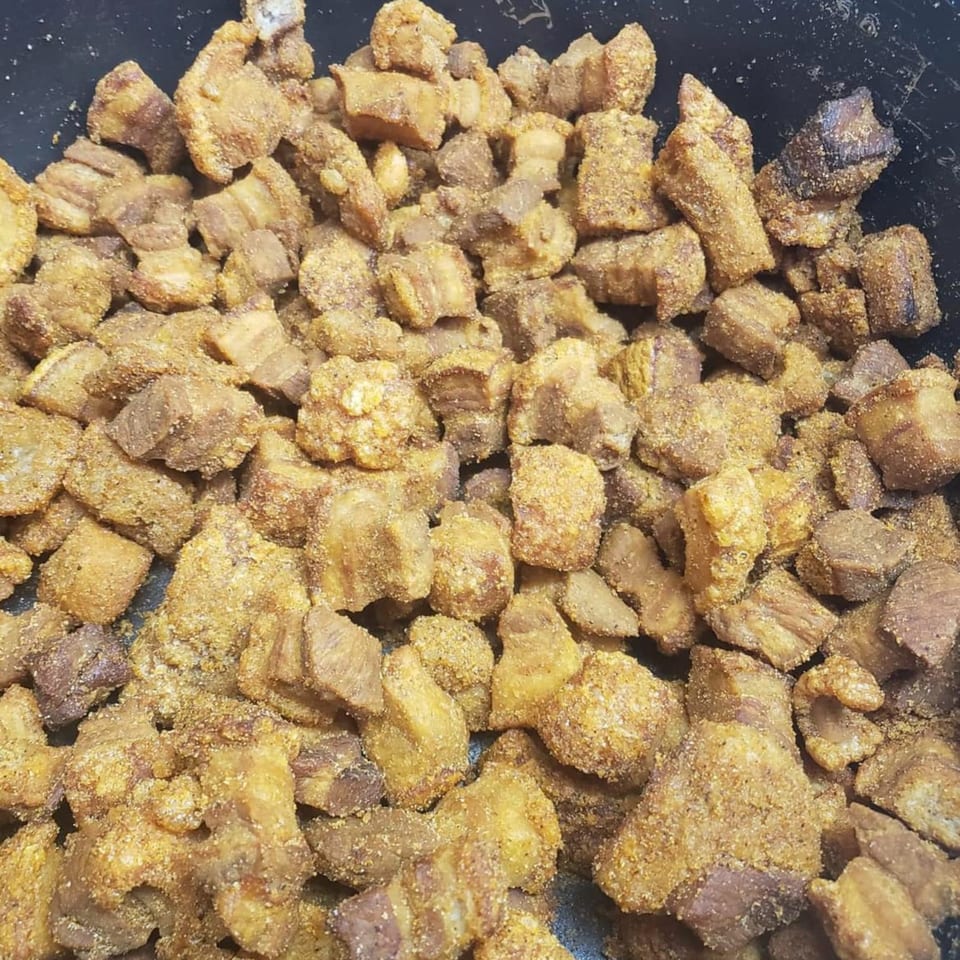 Close-up of golden-brown, seasoned Cajun cracklins, also known as pork rinds, in a dark pan.